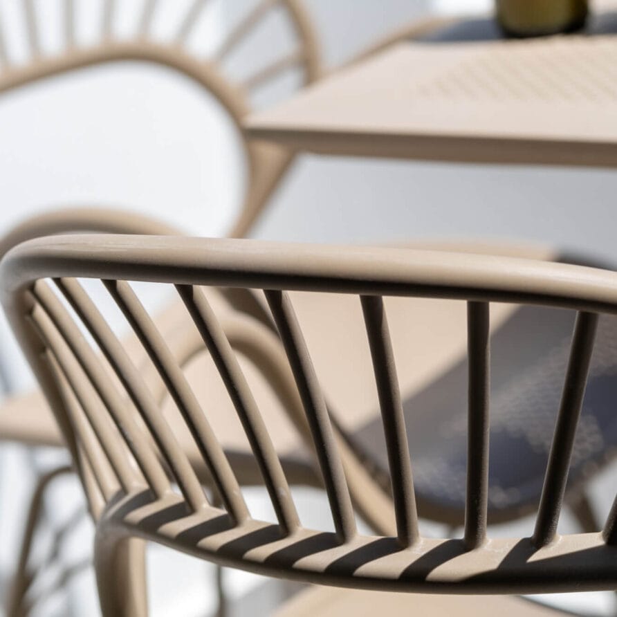 Κοντινό πλάνο μπεζ καρέκλες εξωτερικού χώρου με κάθετες τάβλες δίπλα σε ένα τραπέζι, που όλες ρίχνουν σκιές σε μια φωτεινή επιφάνεια.