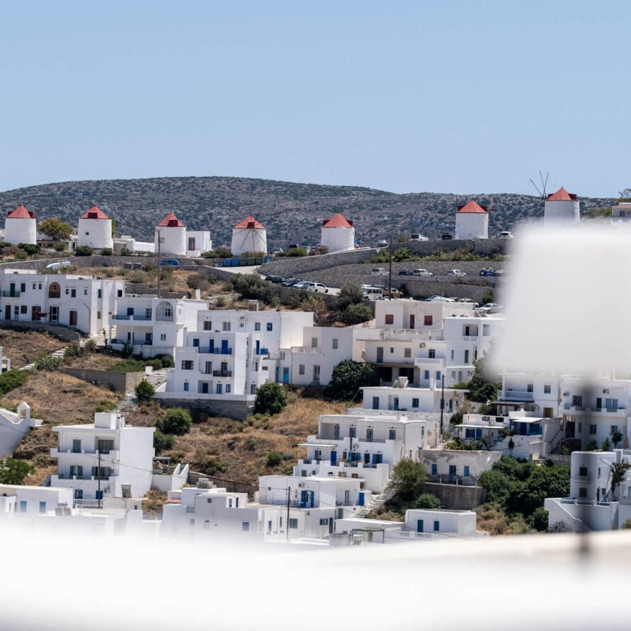 Λευκά κτίρια και ανεμόμυλοι στην πλαγιά ενός λόφου κάτω από έναν καθαρό ουρανό, με μια θολή λάμπα στο προσκήνιο.