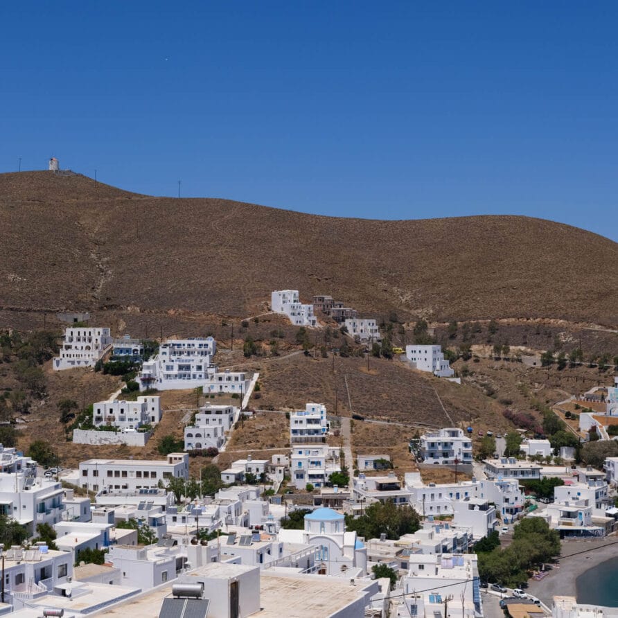 Λευκά κτίρια με επίπεδες στέγες είναι συγκεντρωμένα σε ένα ξηρό, λοφώδες τοπίο κάτω από έναν καθαρό γαλάζιο ουρανό, με ορισμένες κατασκευές διάσπαρτες στην πλαγιά του λόφου.