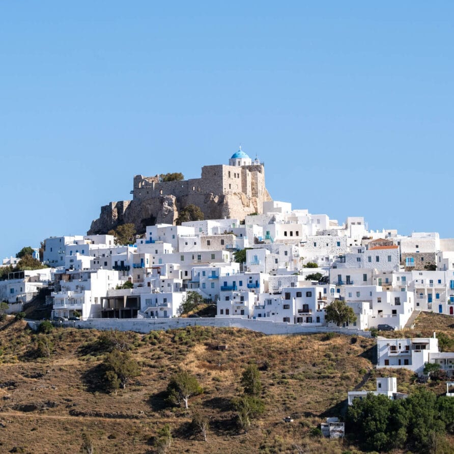 Ένα χωριό στην πλαγιά ενός λόφου με λευκά κτίρια και ένα πέτρινο κάστρο με έναν μπλε τρούλο στην κορυφή, με φόντο έναν καταγάλανο ουρανό.