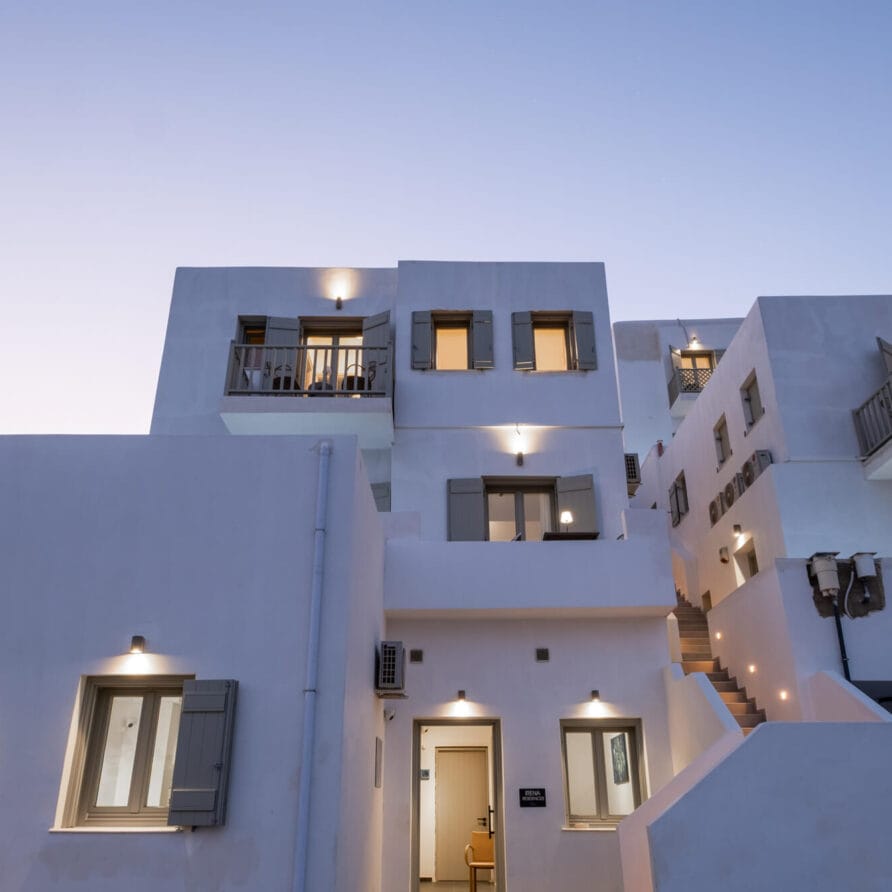 Σύγχρονα λευκά κτίρια με μπαλκόνια και εξωτερικά φώτα που φωτίζονται το σούρουπο, με καθαρές γραμμές και μινιμαλιστικό αρχιτεκτονικό στυλ.