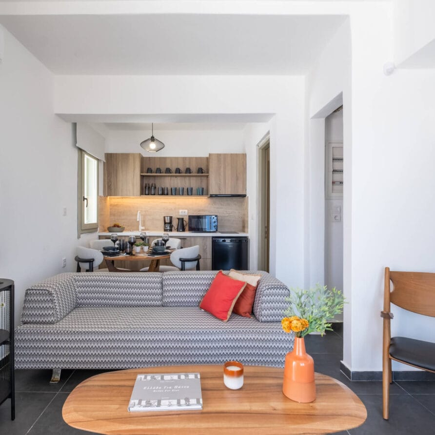 Μοντέρνο σαλόνι με καναπέ με σχέδια, ξύλινο τραπεζάκι σαλονιού, τηλεόραση επίπεδης οθόνης και θέα σε μια κουζίνα με ανοιχτόχρωμα ξύλινα ντουλάπια και τραπεζαρία.