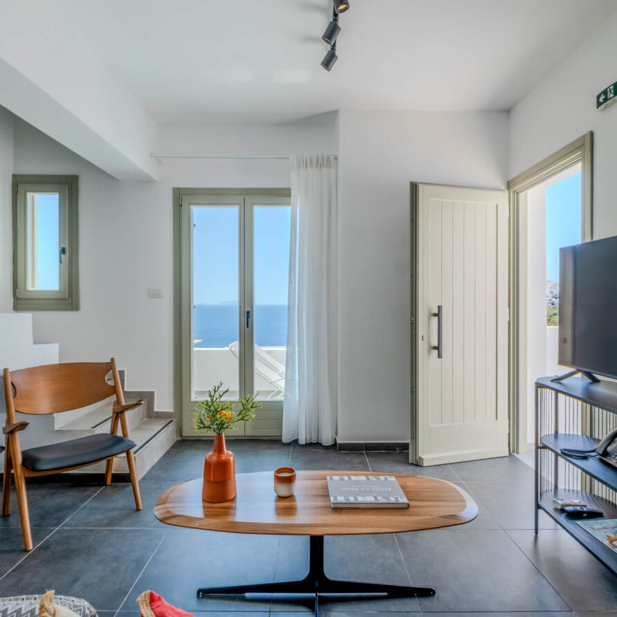 Μοντέρνο σαλόνι με ξύλινα έπιπλα, τηλεόραση επίπεδης οθόνης, σκάλα και μεγάλα παράθυρα με θέα στη θάλασσα.