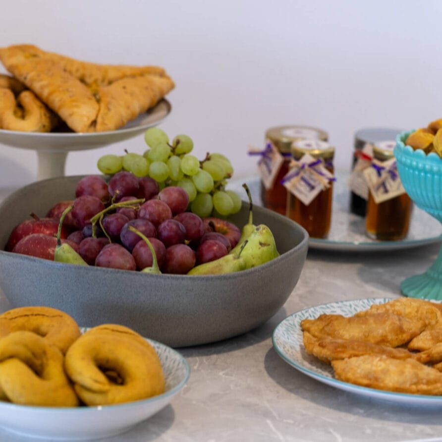 Μια ποικιλία από αρτοσκευάσματα, ένα μπολ με σταφύλια και αχλάδια, βάζα με μαρμελάδα και ένα πιάτο κουμκουάτ είναι τοποθετημένα σε ένα μαρμάρινο τραπέζι.