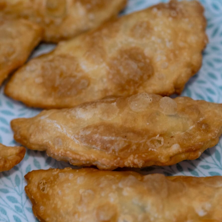 Αρκετές χρυσοκαφέ, τηγανητές εμπανάδας είναι τοποθετημένες σε ένα ανοιχτό μπλε πιάτο με σχέδια.